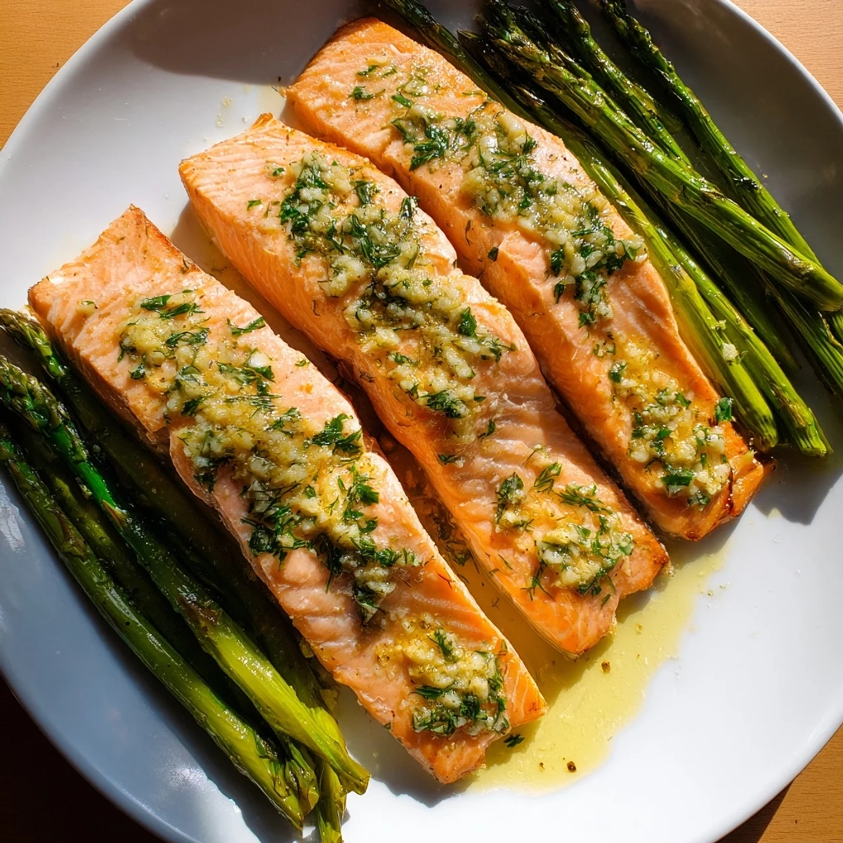 Golden-brown salmon fillets glisten with lemon garlic butter sauce beside vibrant green roasted asparagus spears on a baking sheet.