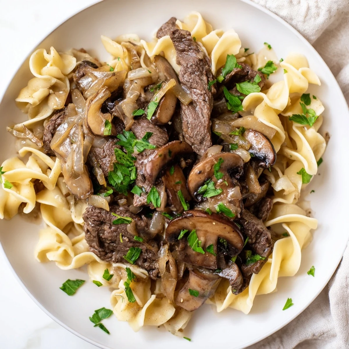 Savory Beef Stroganoff is served hot over a nest of golden egg noodles, garnished with fresh green parsley.