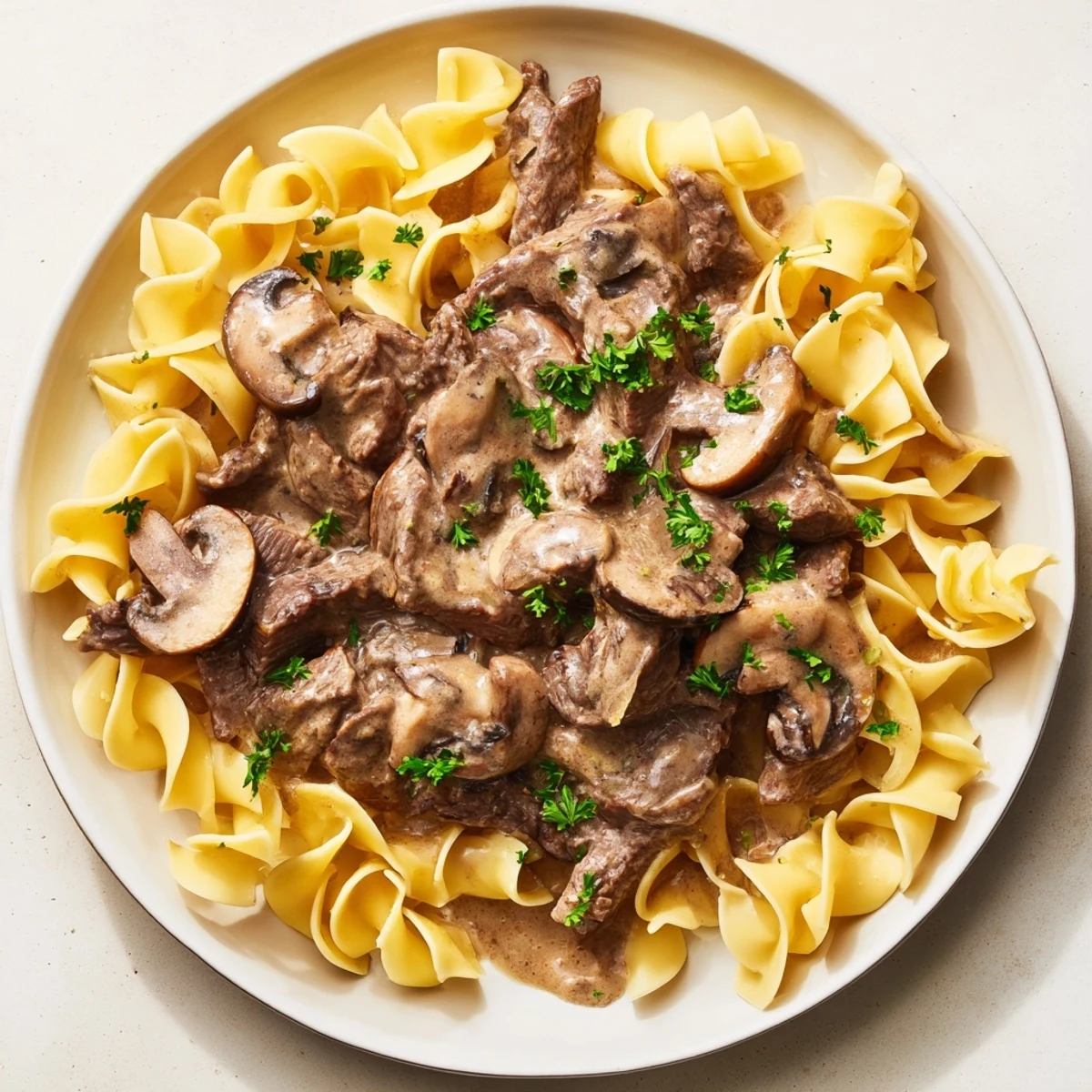 A close-up of classic Beef Stroganoff over egg noodles highlights the rich, velvety sauce and juicy meat pieces.
