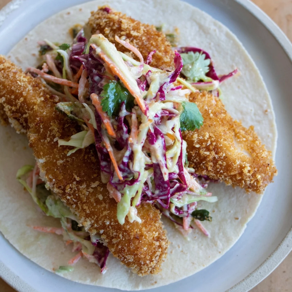 Crunchy panko-coated fish nestled in a soft tortilla with zesty cabbage slaw and creamy drizzle.