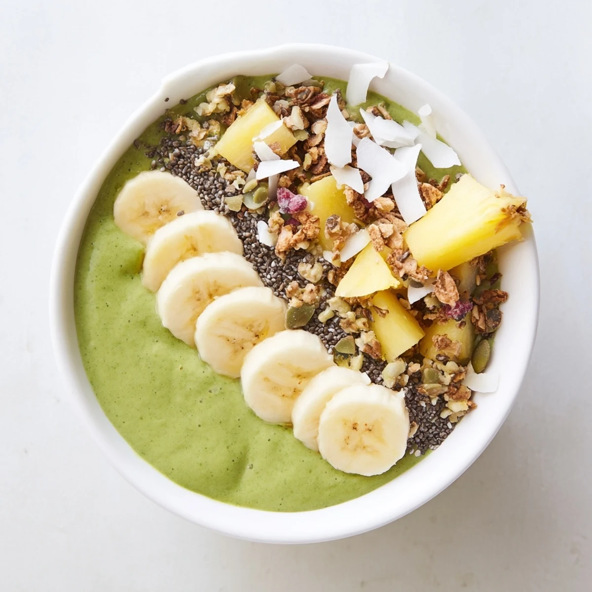 Thick, nutrient-rich Green Smoothie Bowl with Spinach and Pineapple topped with granola, pumpkin seeds, and fresh pineapple chunks.