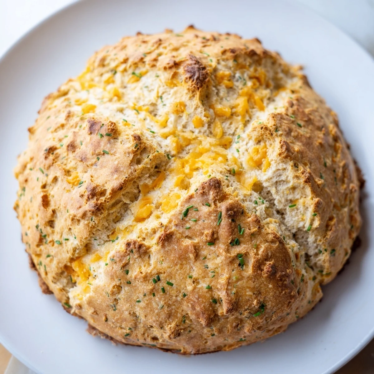 A close-up of Savory Cheddar & Chive Irish Soda Bread with a golden, cheesy crust and tender crumb, sliced to show the melted cheddar flecks and fresh green chives.