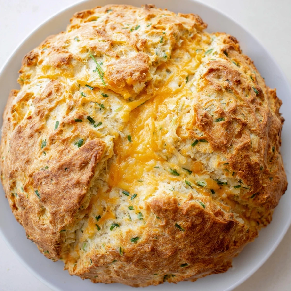 Rustic round Savory Cheddar & Chive Irish Soda Bread cooling on a wire rack with a deep cross cut on top, ready to be served warm with butter for breakfast.