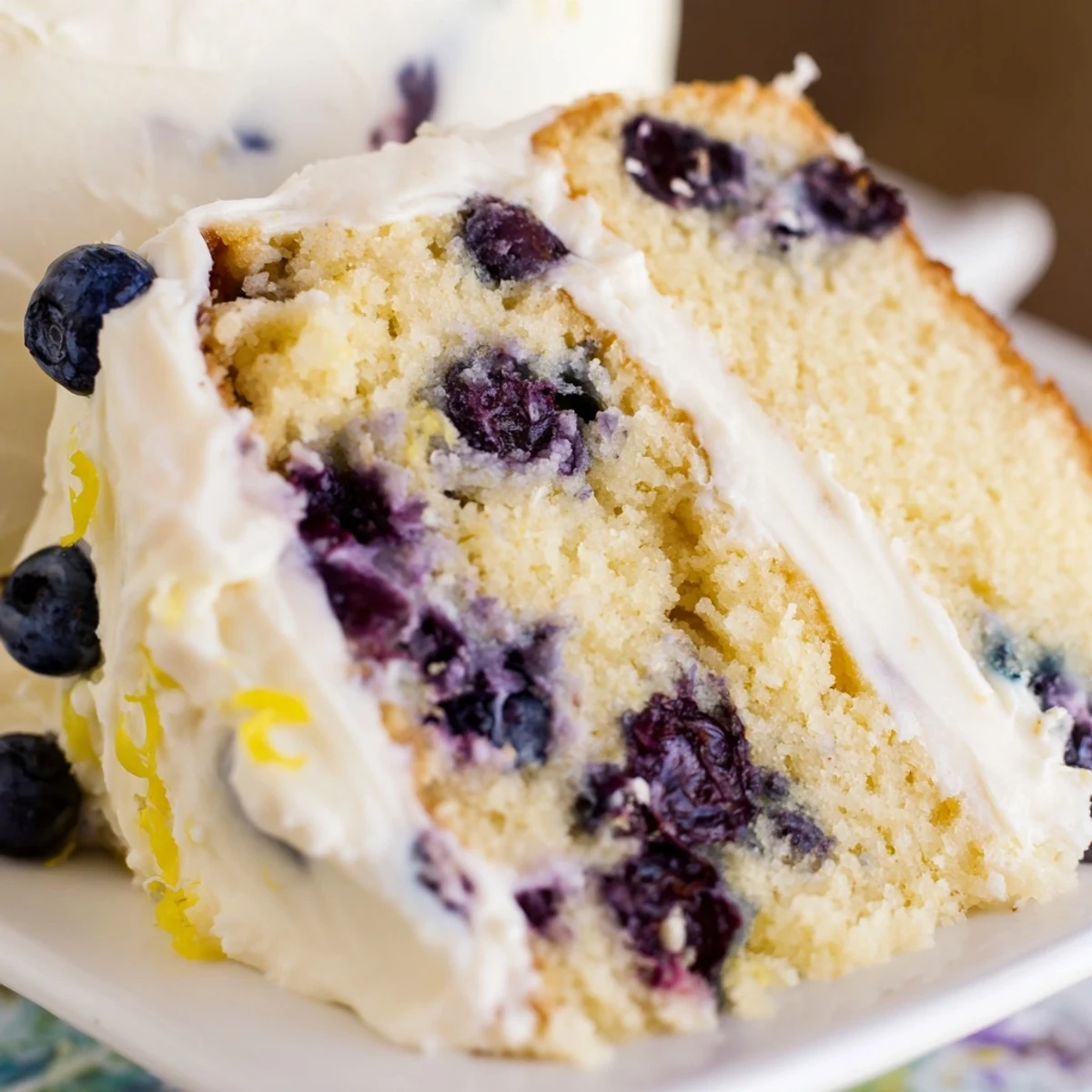 A slice of Lemon Blueberry Cake with Cream Cheese Frosting shows juicy berries and a tangy glaze. 