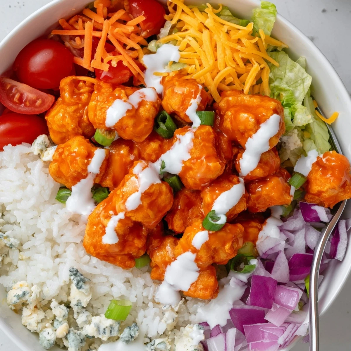 Freshly diced red onions, cherry tomatoes, and melted cheddar cheese top this vibrant Buffalo Chicken Bowls meal.