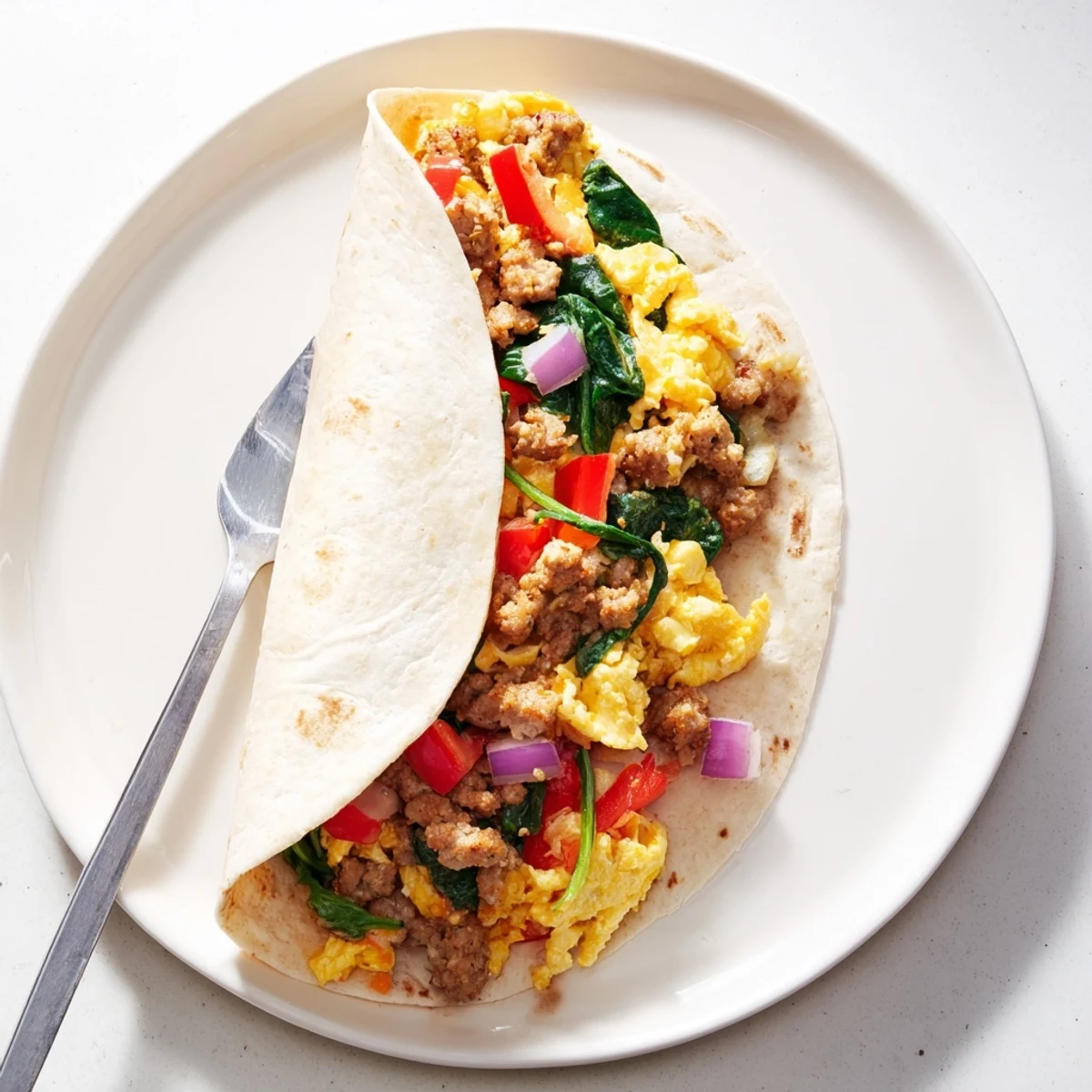 Golden make-ahead breakfast burritos wrapped in foil with fluffy eggs, melted cheddar cheese, and colorful vegetables