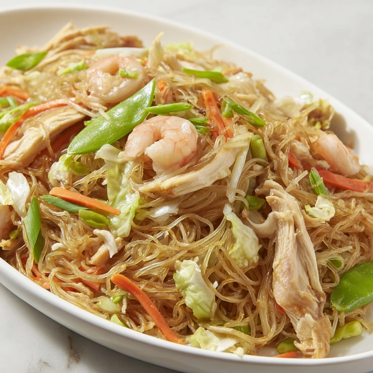 Traditional Pancit Bihon featuring tender rice noodles stir-fried with succulent chicken, shrimp, and colorful vegetables in a savory soy sauce.