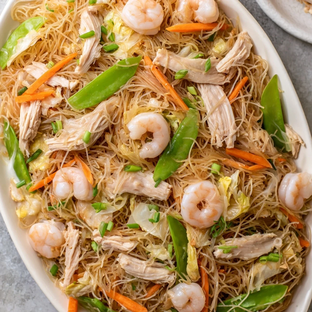 Steaming plate of Pancit Bihon showcasing springy rice noodles coated in rich umami sauce alongside julienned carrots and crisp cabbage.