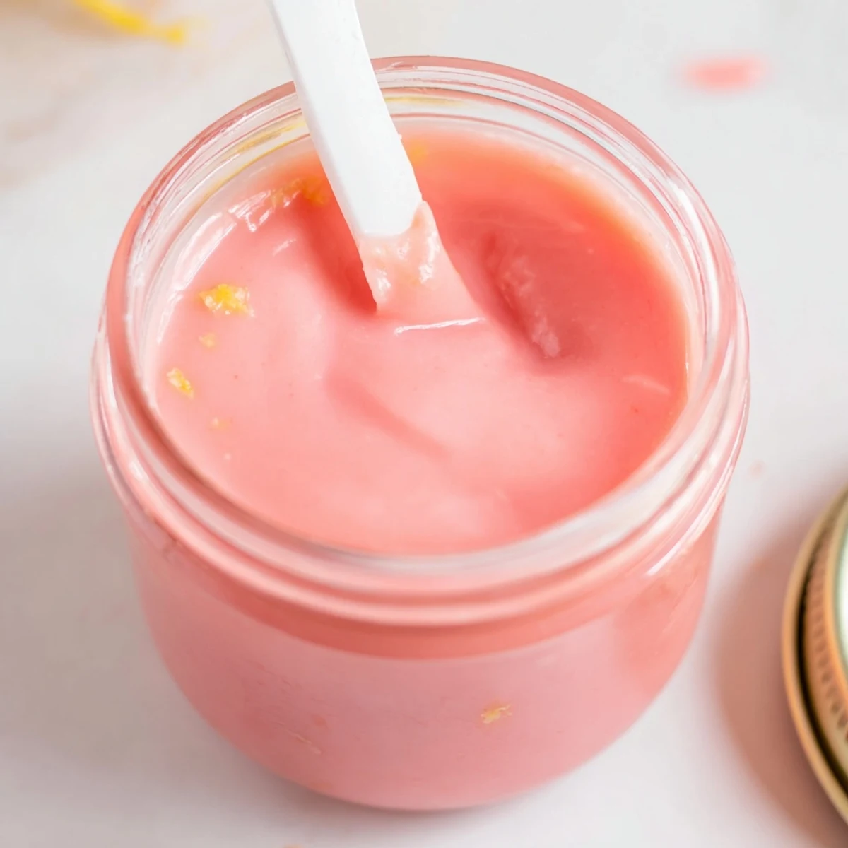 Creamy homemade pink lemon curd served in a glass jar with a small silver spoon