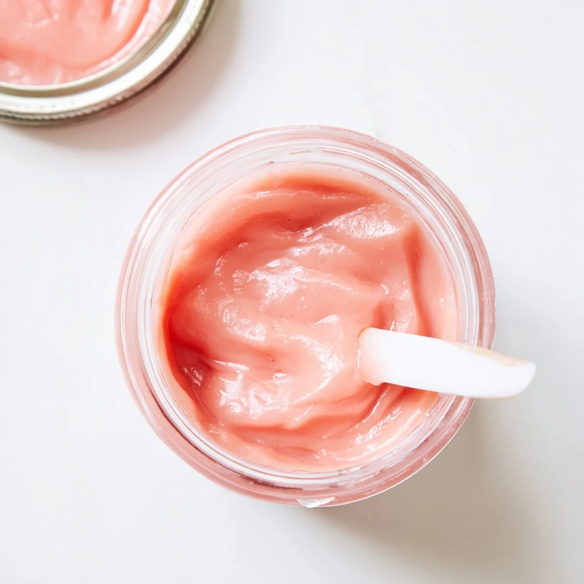 Silky smooth pink lemon curd being drizzled from a whisk into a decorative white bowl