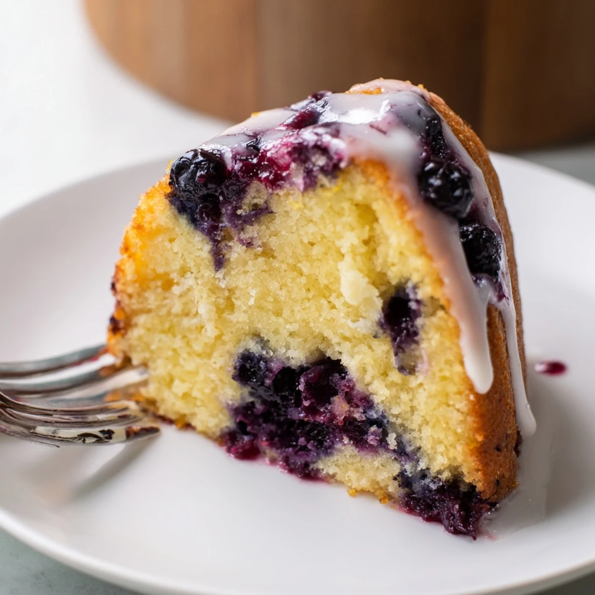 Homemade lemon blueberry cake on a white plate with sweet lemon icing dripping down sides
