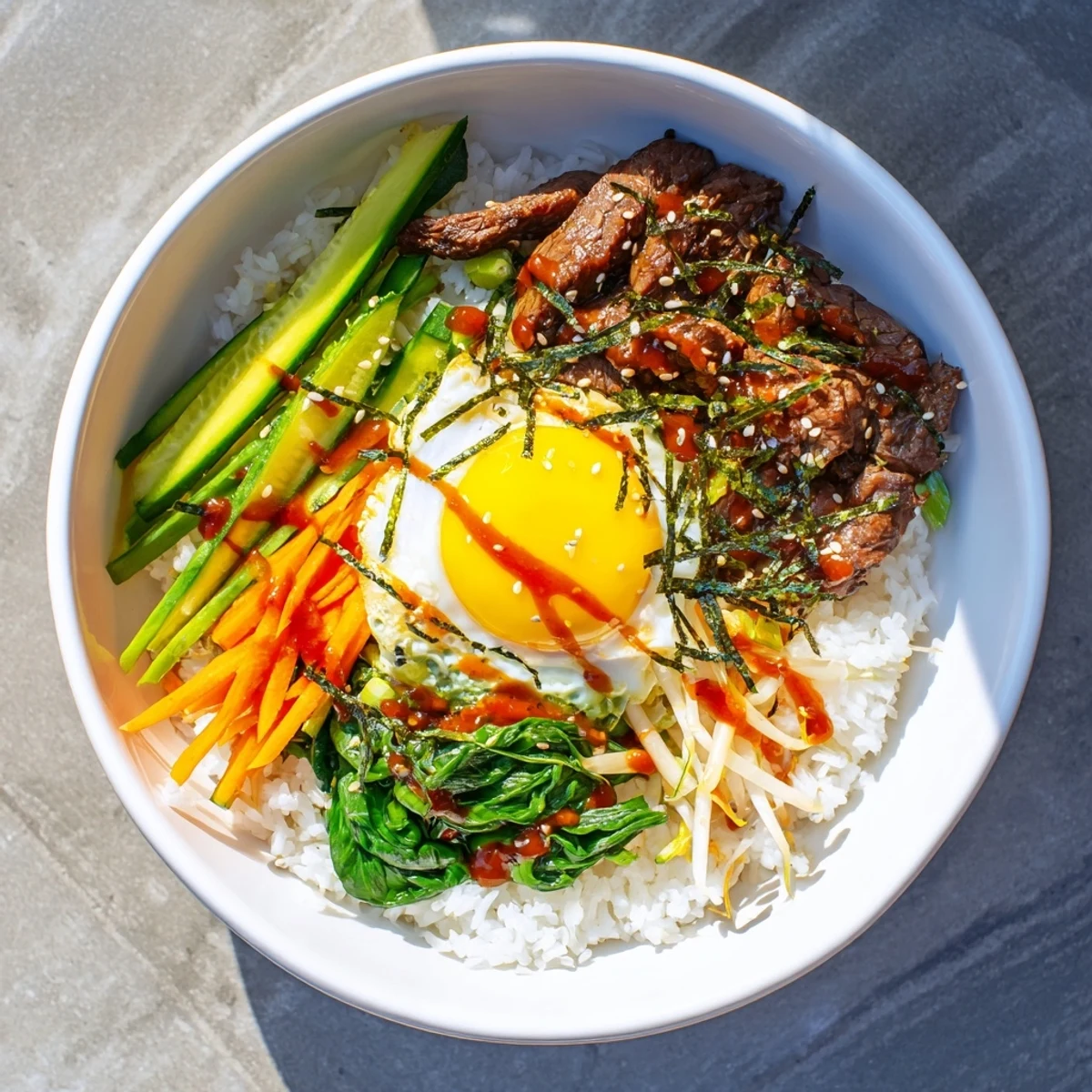 Vibrant Korean-Inspired Breakfast Bowl arranged in sections featuring savory beef, fresh julienned carrots, cucumber, spinach, and a runny yolk.