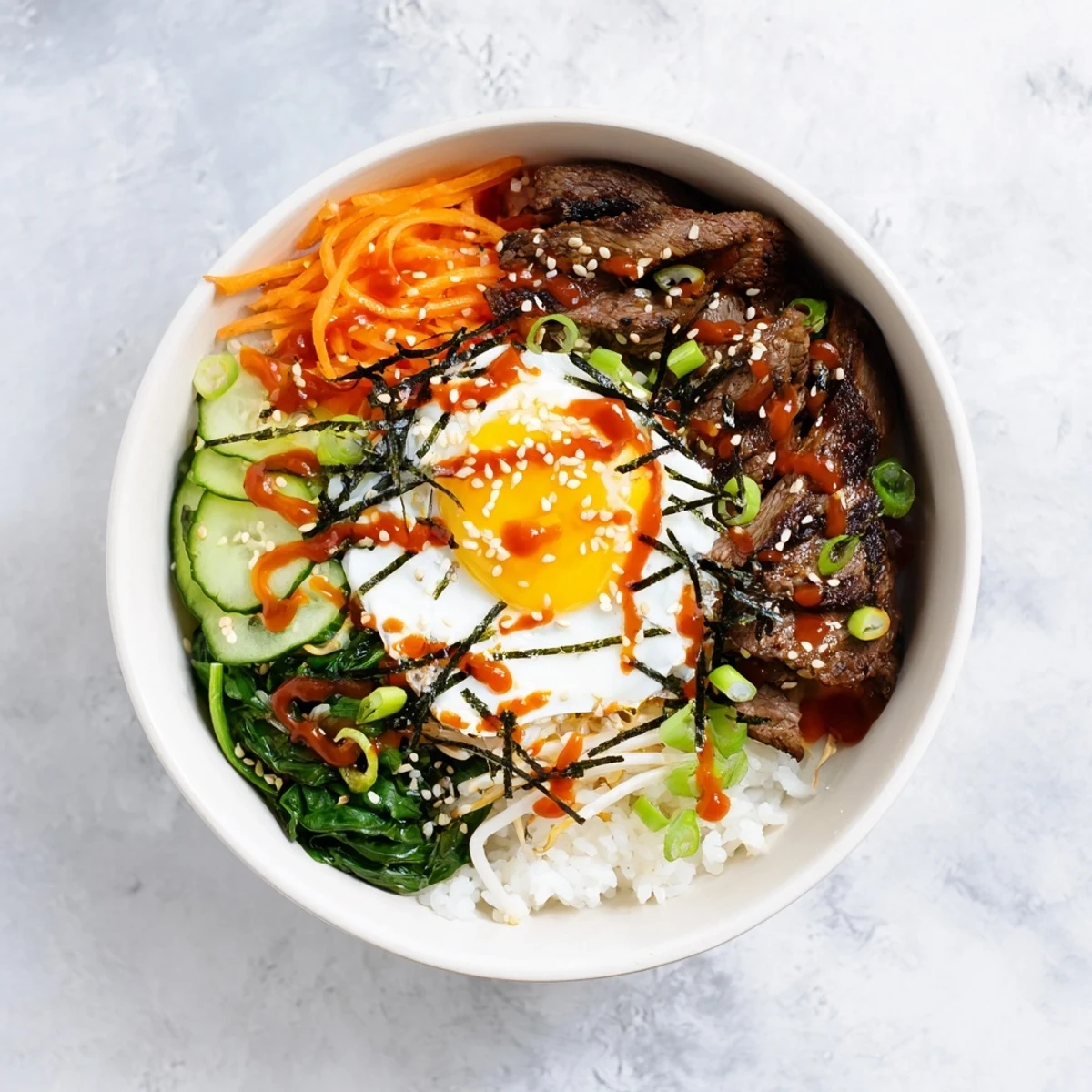 Golden fried egg tops this Korean-Inspired Breakfast Bowl with marinated beef, crisp vegetables, and steamed rice drizzled with spicy gochujang sauce.