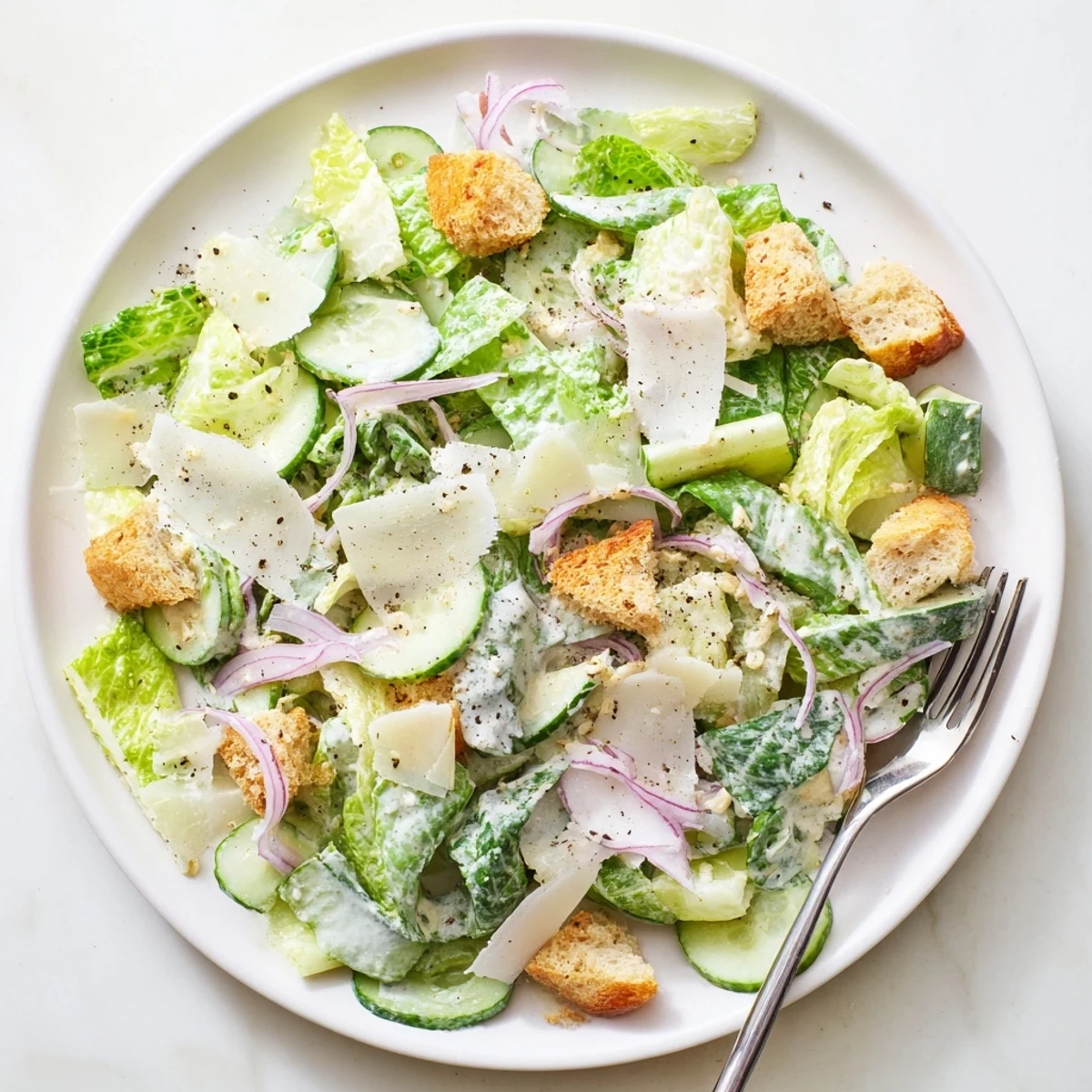 Close-up of refreshing cucumber Caesar salad topped with shaved Parmesan and pepper on a rustic wooden table