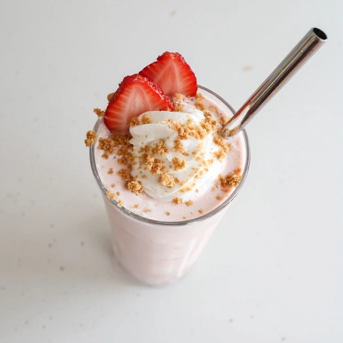 Tall glass of strawberry cheesecake milkshake topped with whipped cream and fresh strawberry slices