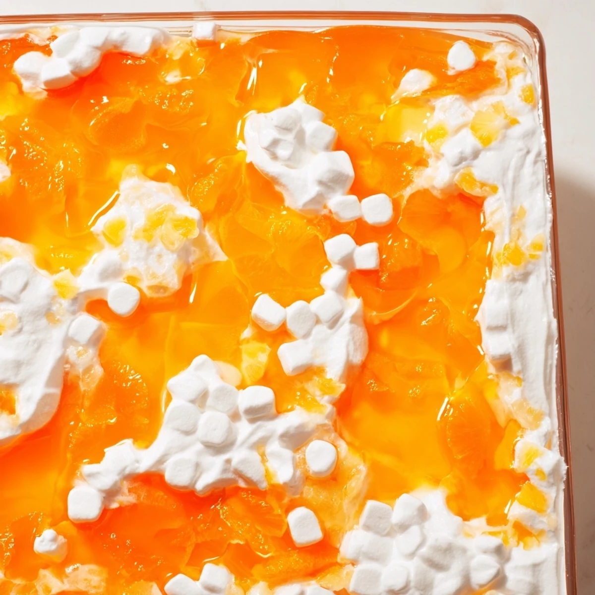 Vibrant orange Jell-O salad with mandarin oranges and pineapple in a glass serving dish