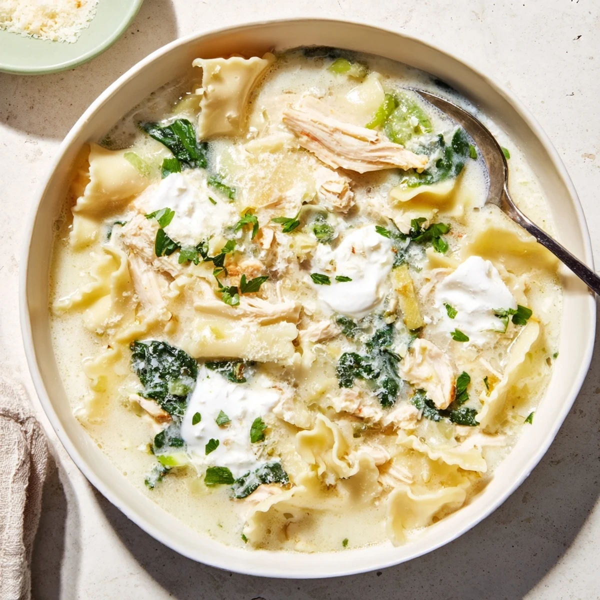 Steaming bowl of white lasagna soup featuring spinach chicken and broken lasagna noodles swimming in rich Italian broth
