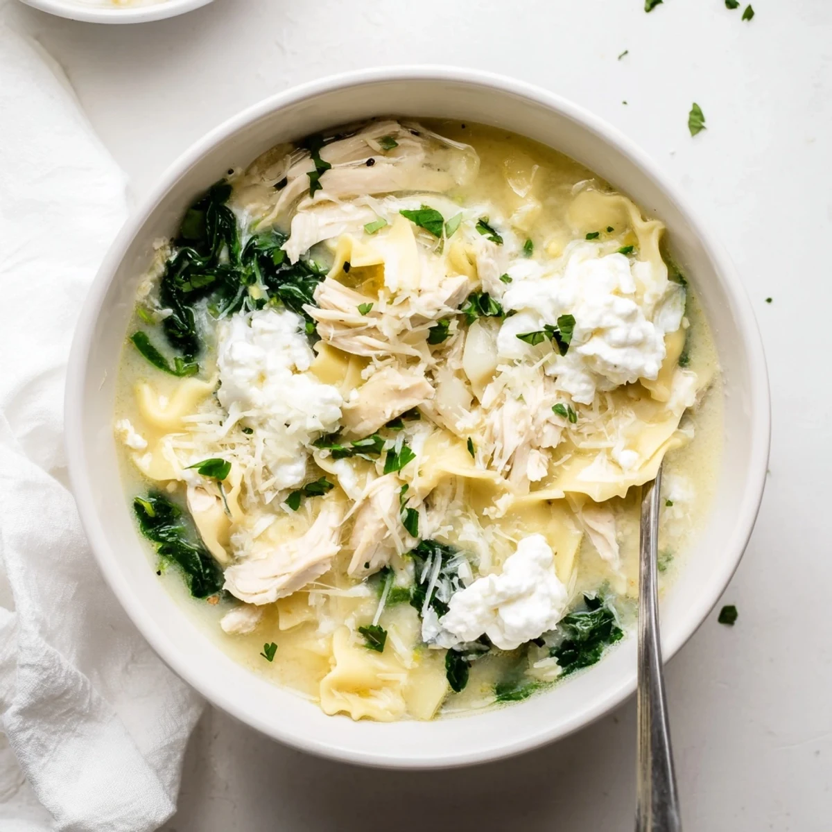 Garnished white lasagna soup with shredded chicken and parmesan cheese served in rustic bowl with fresh parsley