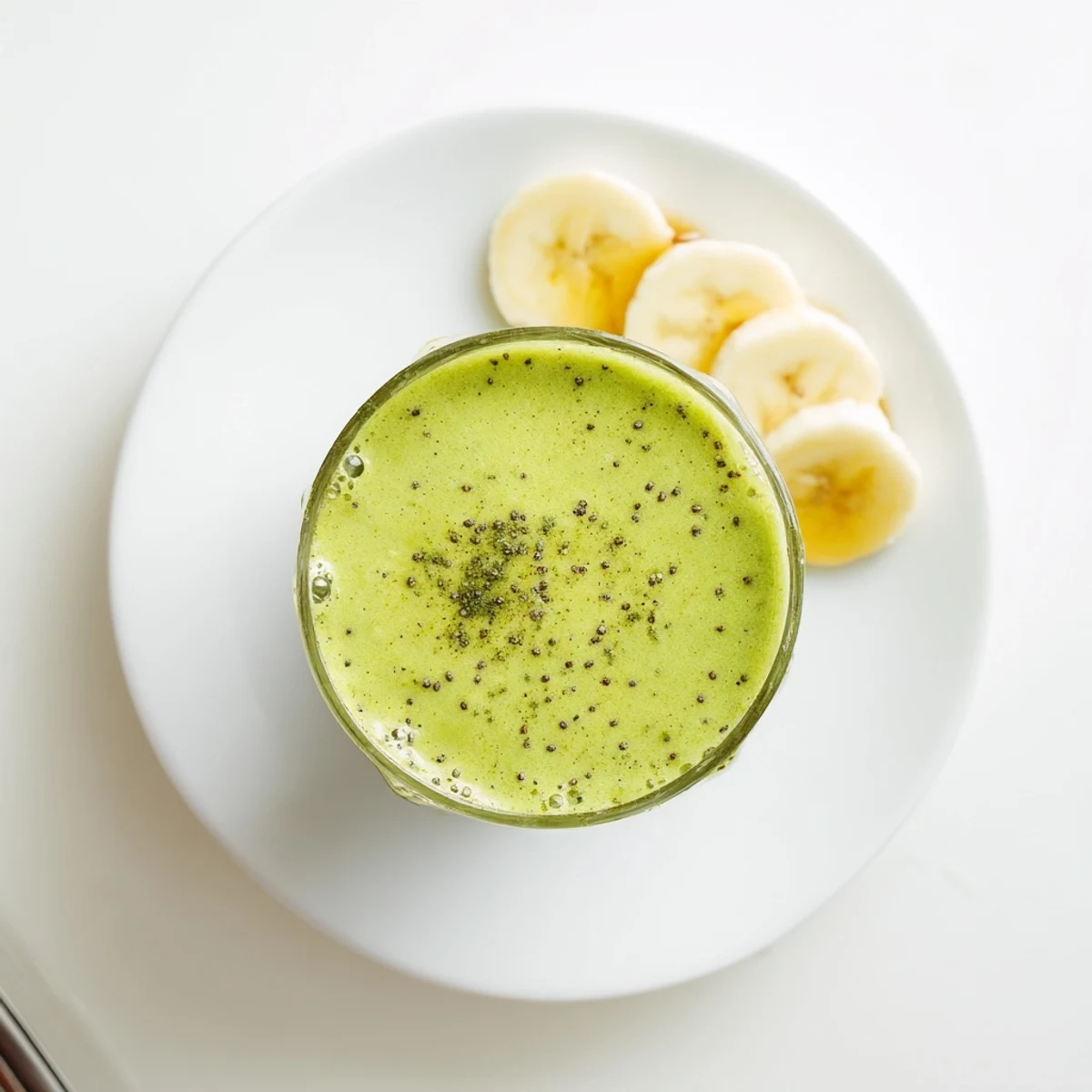 Creamy energizing banana matcha smoothie poured into a glass with vibrant green swirls and frothy texture