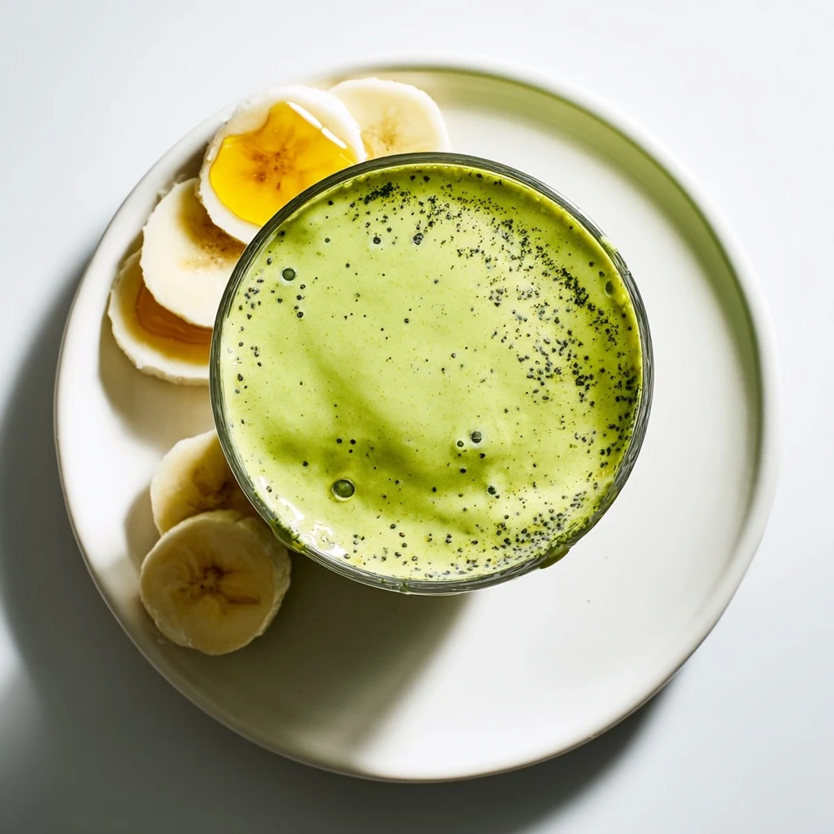 Thick energizing banana matcha smoothie topped with chia seeds in a clear glass showing layers