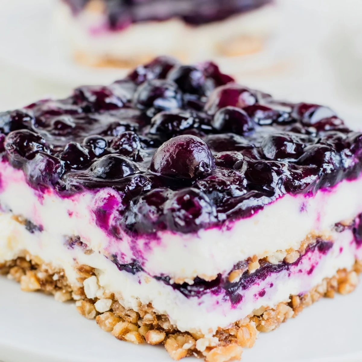 Festive sweet and tangy blueberry jamboree dessert with glossy purple berry topping layered over creamy white cheesecake filling and golden pecan crust