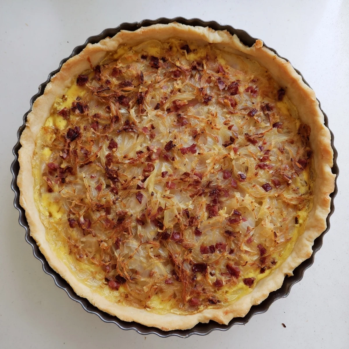 Homemade German onion pie baked in a white dish served with fresh green salad on wooden table