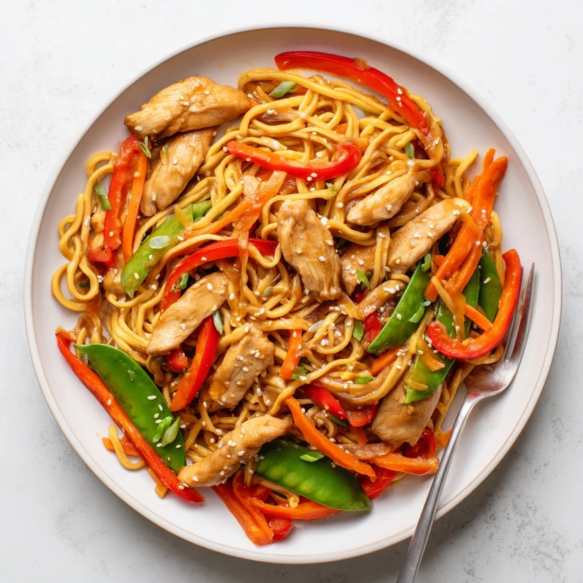 Close-up of sticky garlic chicken noodles tossed in rich caramelized glaze with scallions