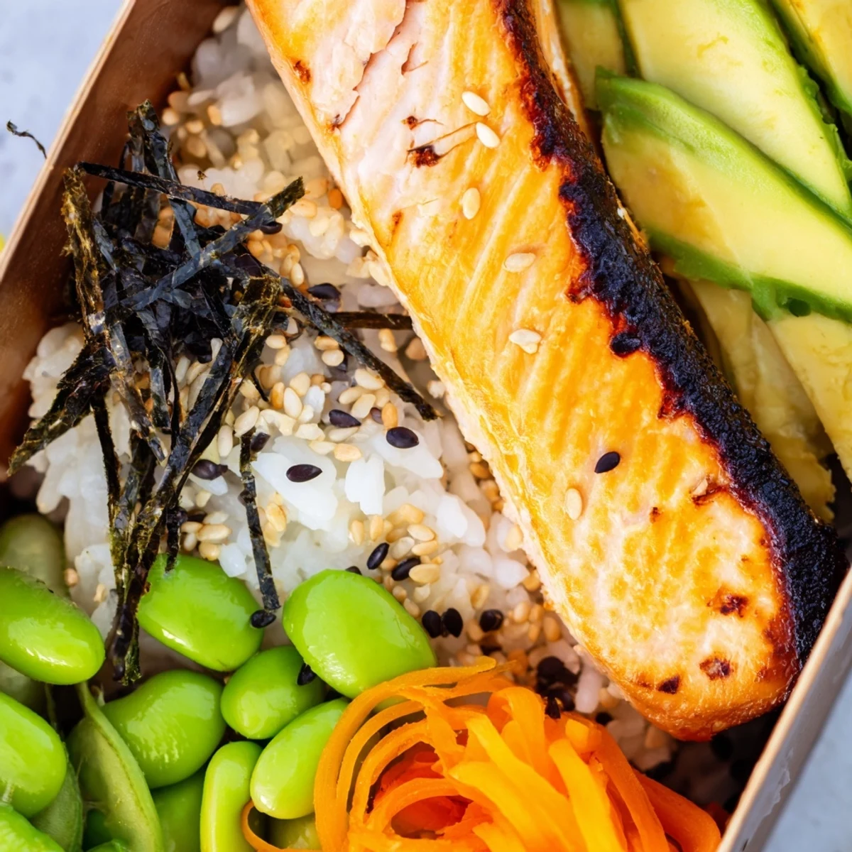 Nourishing Japanese-style breakfast bento showcasing grilled fish, egg, avocado slices, edamame, and steamed rice with sesame seeds