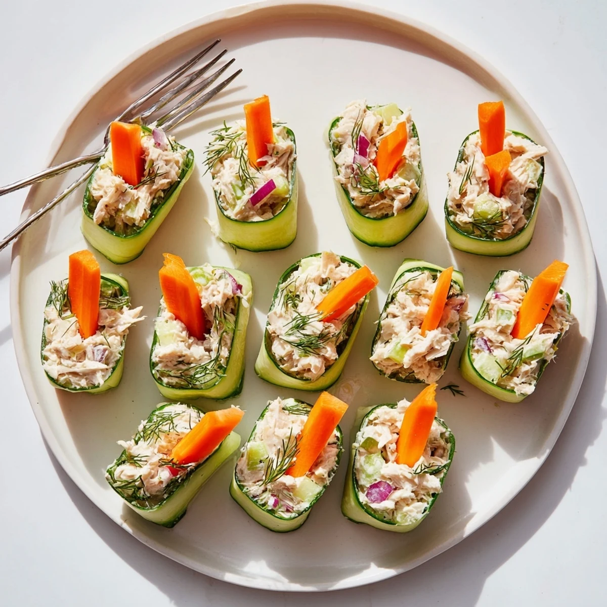 Bite-sized chicken salad cucumber roll ups arranged on white serving platter
