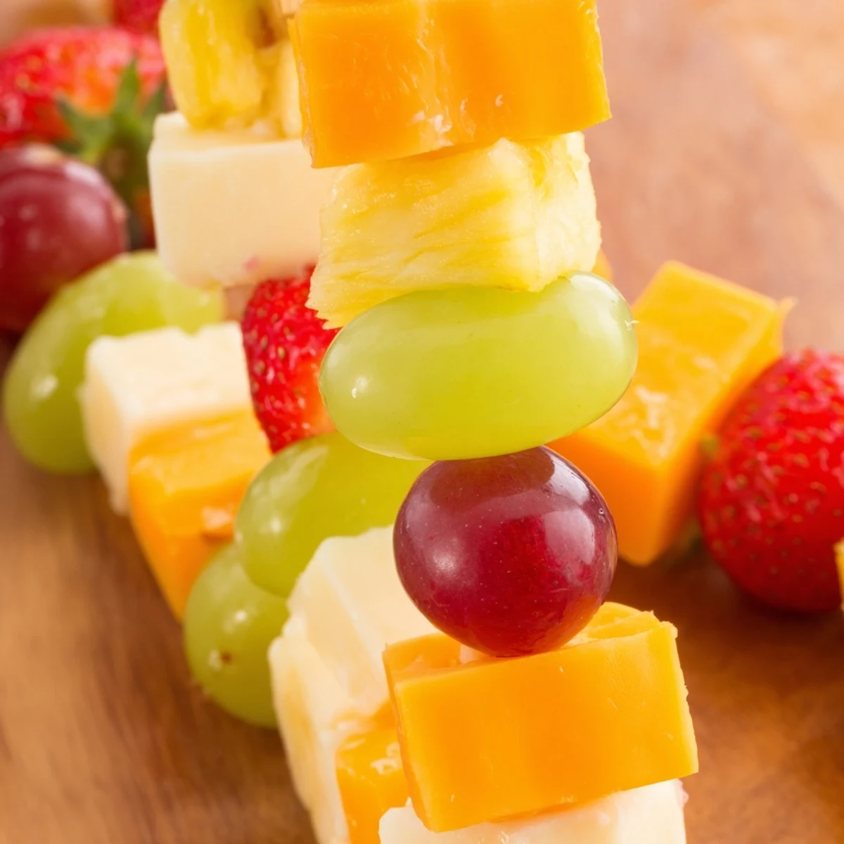 Colorful fruit and cheese kabobs arranged on a platter with grapes, strawberries, pineapple, and cheddar cubes