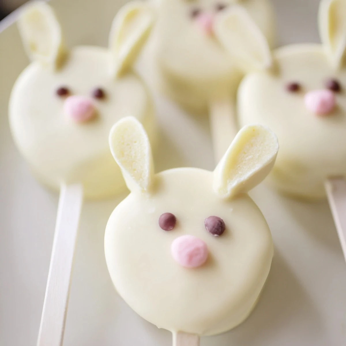 Creamy white chocolate bunny cakesicles with candy eyes on a rustic serving board for Easter.