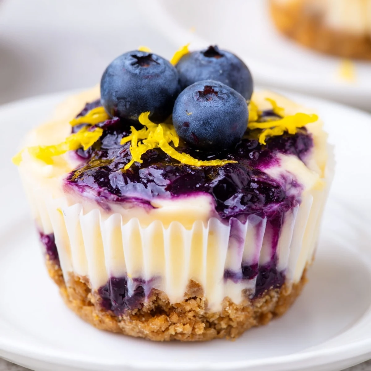 Tangy mini lemon blueberry cheesecakes garnished with fresh berries and bright lemon zest