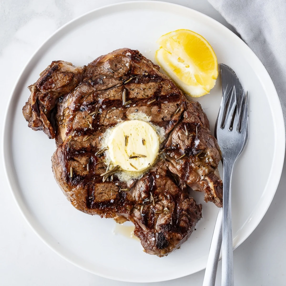 Tender grilled steak topped with melting butter served with lemon wedges on a rustic wooden platter