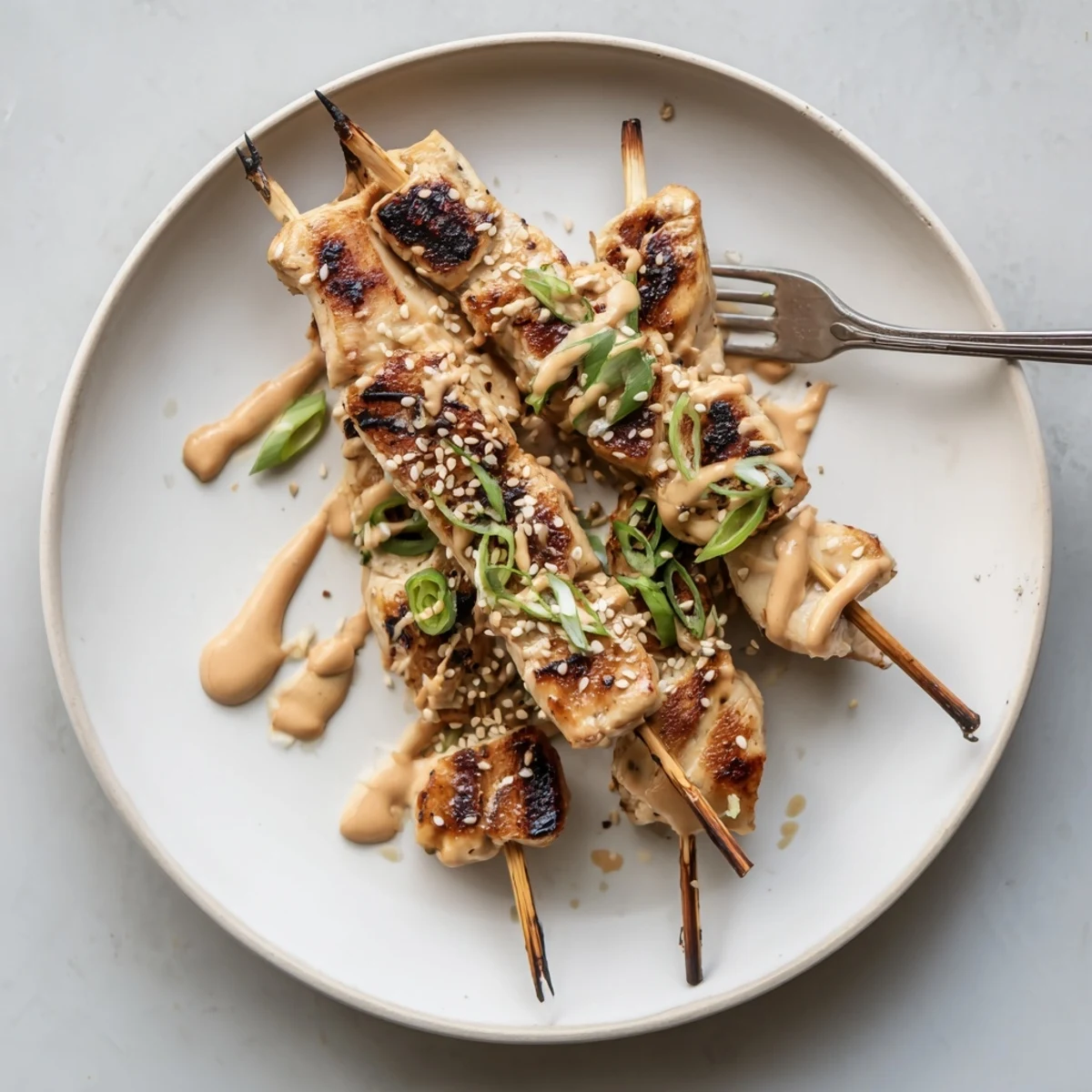 Juicy Bang Bang Chicken skewers on a platter topped with green onions and white sesame seeds