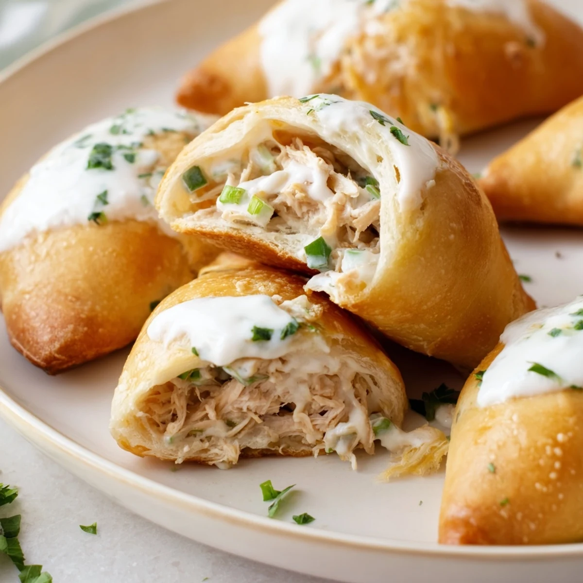 Flaky pastry-wrapped chicken pillows served warm on a plate with velvety parmesan cream sauce