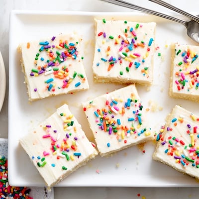 Sugar cookie bars stacked on a wooden cutting board next to a glass of milk.