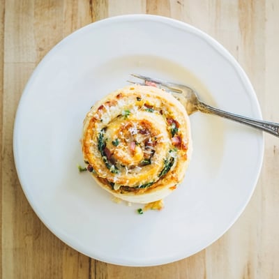 A close-up of a Savory Spinach and Ham Breakfast Roll shows flaky, golden layers with melted cheese and green onions.