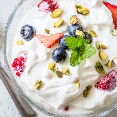 Close up shot of Fluffy Yogurt Cloud Dessert with Berries and Cream garnished with fresh mint and chopped pistachios on top.