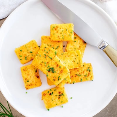Crispy cheddar chive snack bites glowing golden beside a bowl of dip