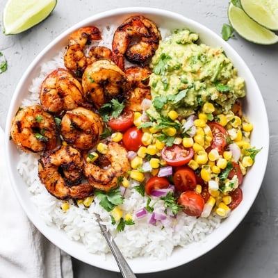 Grilled shrimp bowl with avocado corn salsa topped with fresh lime wedges